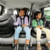 Two children sit in their car seats in the back of a vehicle.