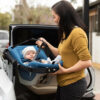 A woman is holding the handle of her baby in a car seat.